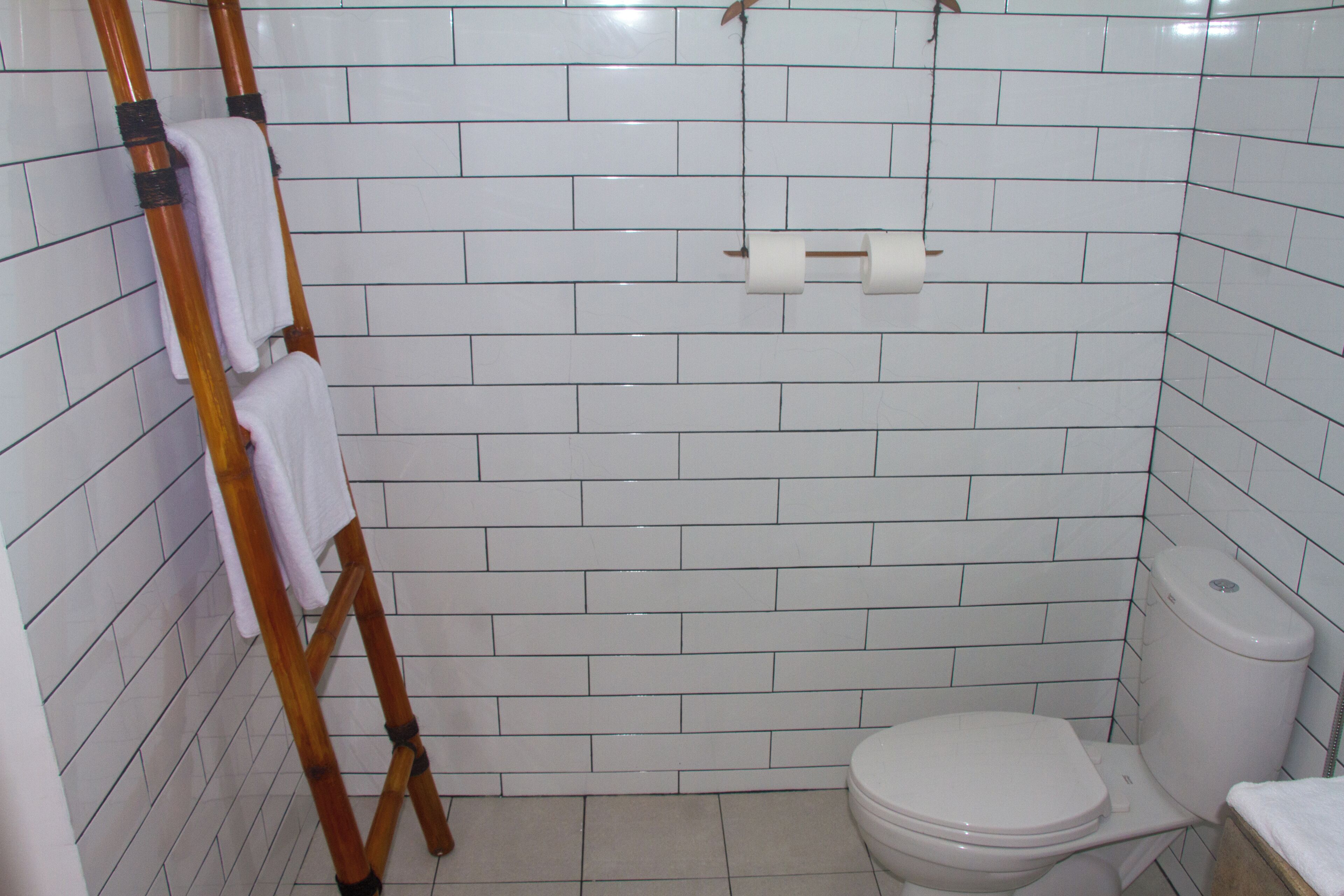 Une salle de bain avec des murs recouverts de carreaux blancs, une échelle en bois, des toilettes et un porte-serviettes.