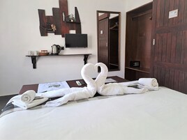 Egy gondosan megterített ágy, rajta hattyúmotívumos törölközővel, a falon egy televízió, egy fa ajtó, és egy polc, rajta egy vízforralóval és csészékkel.
