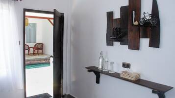 Una habitación con una puerta que da a un balcón, un estante de madera con botellas y pañuelos, y un estante en la pared con una bicicleta y un adorno.