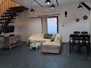 Een moderne woonkamer met een bank, een bijzettafeltje, een televisie, een trap en een eethoek.