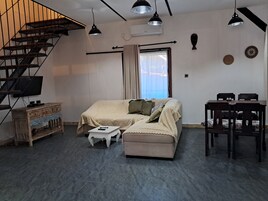 Una sala de estar moderna con sofá, una mesita, televisor, escalera y comedor.
