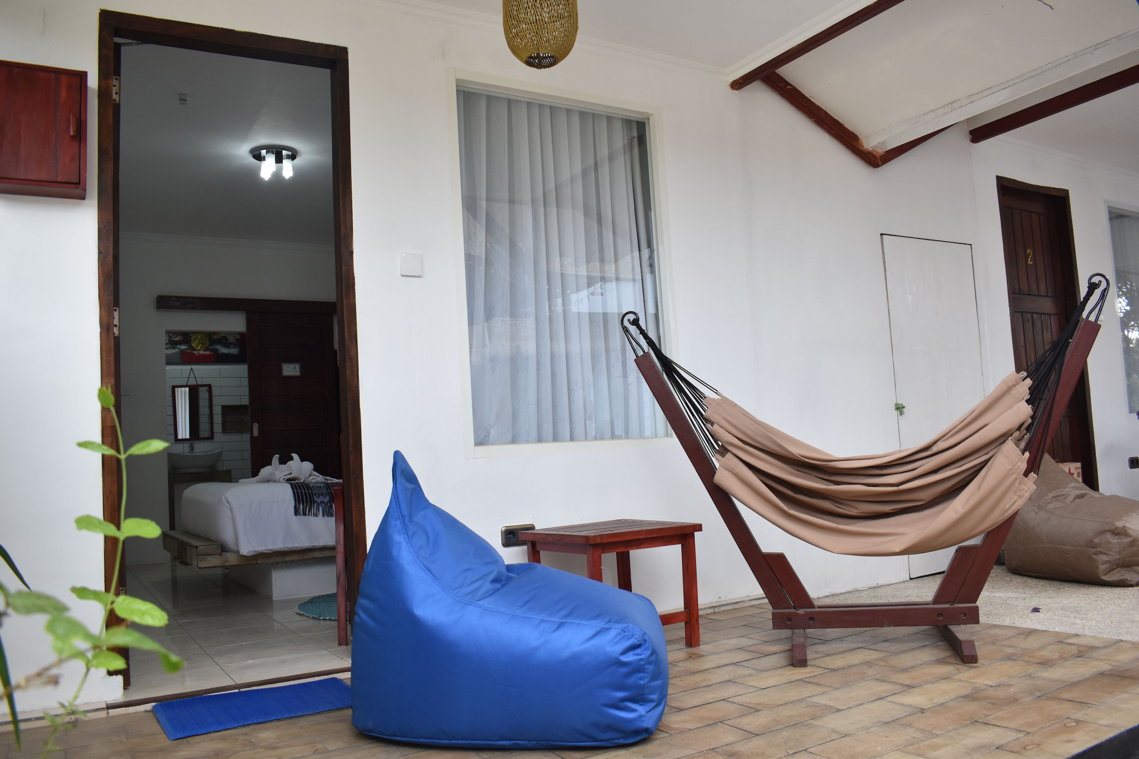 Quarto com rede, um puf azul, uma mesa pequena e uma porta para outro espaço.