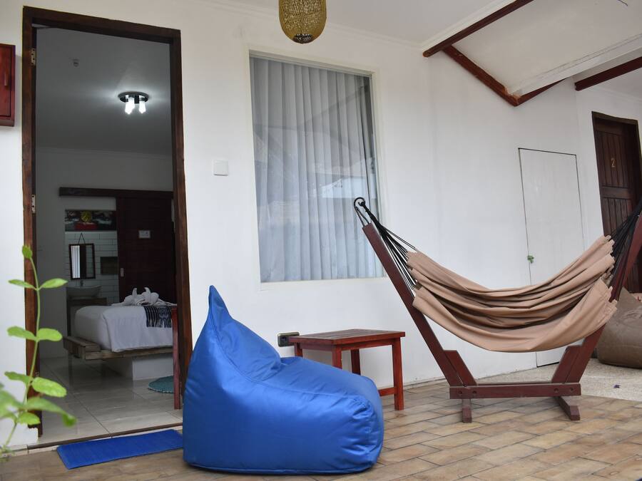 Quarto com rede, um puf azul, uma mesa pequena e uma porta para outro espaço.