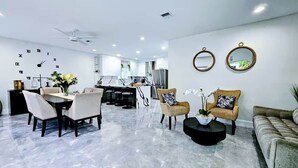 A modern living room with a dining area, a kitchen in the background, and two wall-mounted mirrors.