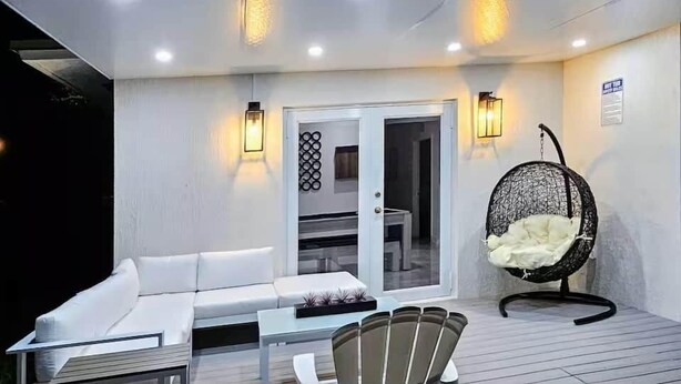 A modern outdoor seating area with a white sofa, a dining table, and a hanging chair.