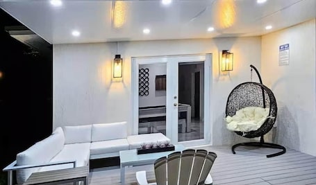 A modern outdoor seating area with a white sofa, a dining table, and a hanging chair.