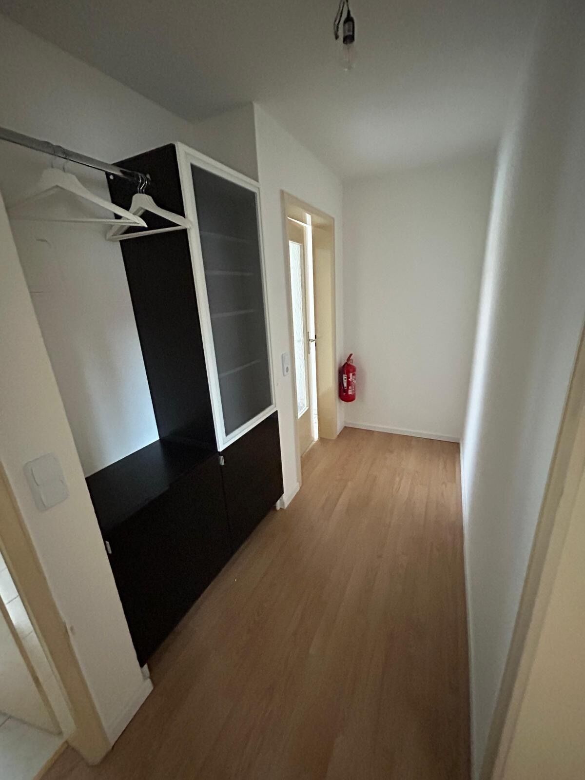 Ein Zimmer mit einem schwarz-weißen Kleiderschrank, einem Feuerlöscher und Holzdielen.