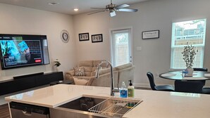A modern kitchen with a dishwasher, a sink with a dish rack, a ceiling fan, and a dining area with a table and chairs. - Walk to Beach | Family-Friendly 3BR Home w/ Garage (Biloxi)