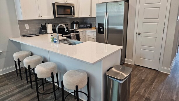 A kitchen with white cabinets, a stainless steel refrigerator, a microwave, a coffee maker, and a sink with stools. - Walk to Beach | Family-Friendly 3BR Home w/ Garage (Biloxi)