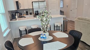 A modern kitchen with white cabinets, a stainless steel refrigerator, and a dining area with a round table and black chairs. - Walk to Beach | Family-Friendly 3BR Home w/ Garage (Biloxi)