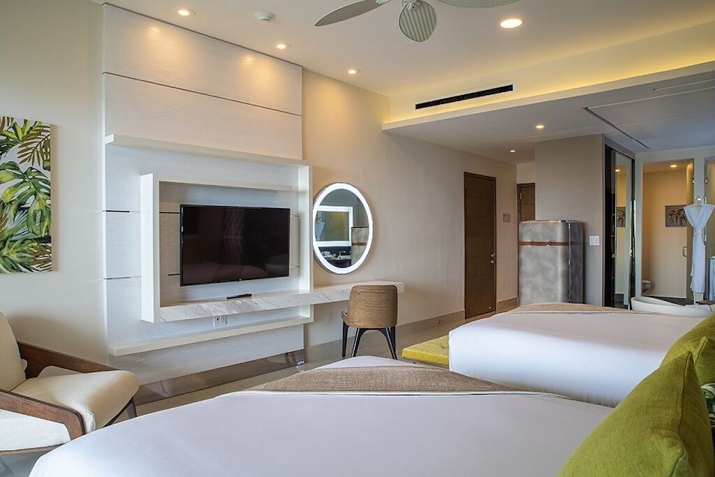 Een moderne hotelkamer met een flatscreen televisie, een ronde spiegel, twee bedden, een stoel en een kleine tafel.