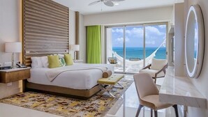 Ein Hotelzimmer mit einem Bett, einem Schreibtisch, einem Sessel, einem großen Fenster mit Meerblick und einem Deckenventilator.