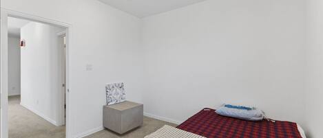 Ein Schlafzimmer mit Bett, Nachttisch, Stuhl und einer Tür zu einem weiteren Raum.