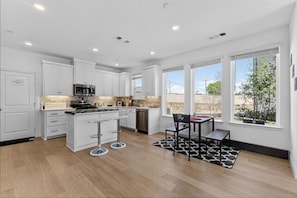 Une cuisine moderne avec des meubles blancs, un îlot central et un coin repas agrémenté d’un tapis noir et blanc.
