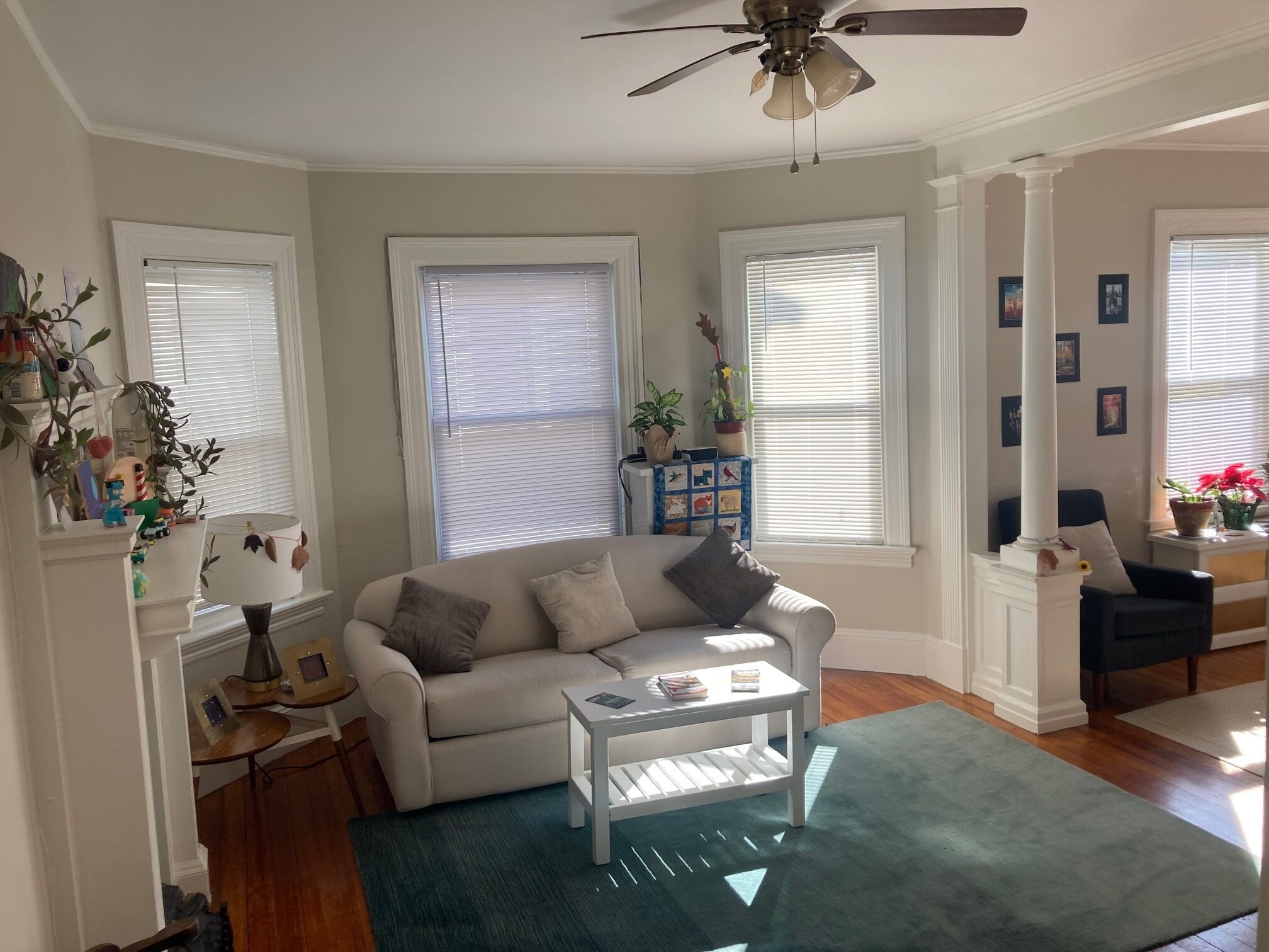 A living room with a white sofa, a coffee table, a ceiling fan, and a window with blinds.