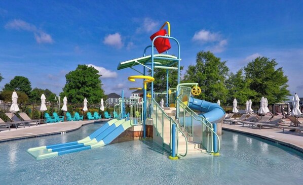 A water park with a blue slide, a red flag, and a pool area with lounge chairs. - NEW - Spacious Delaware Stunner with Panoramic Golf Course Views (Millsboro)