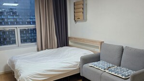 Una camera d'albergo con un letto, un divano grigio, una finestra con tende e un condizionatore d'aria a muro.