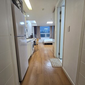 A compact hotel room with a kitchenette, a bed, a window with a view, and a door leading to another room.