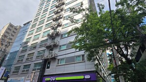 Un edificio a più piani con una vetrina che reca l'insegna 'CU' e un furgone per le consegne parcheggiato di fronte.