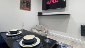 A modern living room with a dining table set for two, a flat-screen TV mounted above a fireplace, and a poster on the wall. - Stylish 2BR Duplex - Central & Spacious (Sunderland)