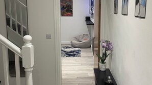 A hallway with a staircase, a bean bag chair, a small table with a plant, and framed artwork on the wall. - Stylish 2BR Duplex - Central & Spacious (Sunderland)