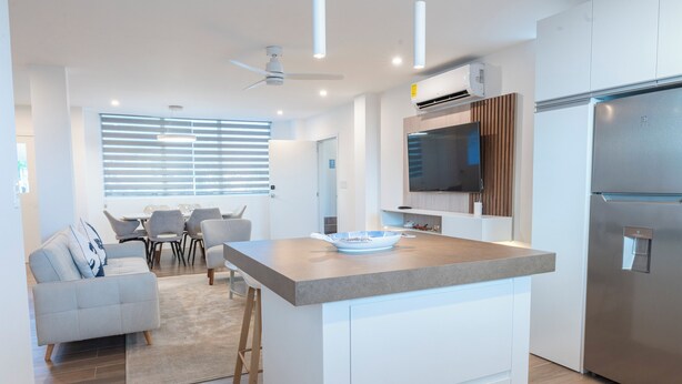 Una cocina moderna con una isla central, electrodomésticos integrados y un comedor con sofá y sillas.