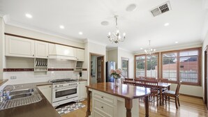 A kitchen with white cabinets, a central island, a dining area with wooden chairs, and large windows. - The Ultimate Holiday Haven: 2 Party Spaces & Bar! (Clyde)