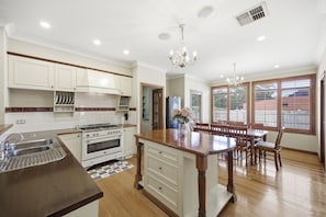 A kitchen with white cabinets, a central island, a dining area with wooden chairs, and large windows.