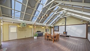 A spacious covered patio with a wooden table and chairs, a grill, hanging plants, and a fireplace. - The Ultimate Holiday Haven: 2 Party Spaces & Bar! (Clyde)