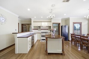 Una cocina amplia con una isla central, mesa de comedor de madera y sillas, muebles blancos y un reloj en la pared.