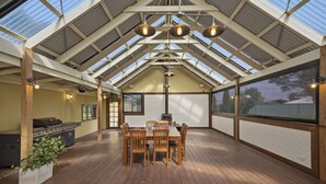 A covered patio with a wooden table and chairs, a grill, and hanging lights. - The Ultimate Holiday Haven: 2 Party Spaces & Bar! (Clyde)