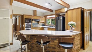 A kitchen with a central island, wooden cabinets, and a view to the outside. - Huge Clyde Holiday Propery: 2 Houses/Bar/BBQ/Pool (Clyde)