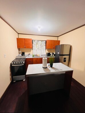 A compact kitchen with wooden cabinets, a stove, a refrigerator, and a small island with a plant. - Located in Flowers Bay, enjoy what this 1-bedroom villa. (Flowers Bay)