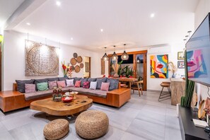 Ein modernes Wohnzimmer mit einer Eckcouch, einem Holztisch als Couchtisch und einem Essbereich mit Holztisch und Stühlen.