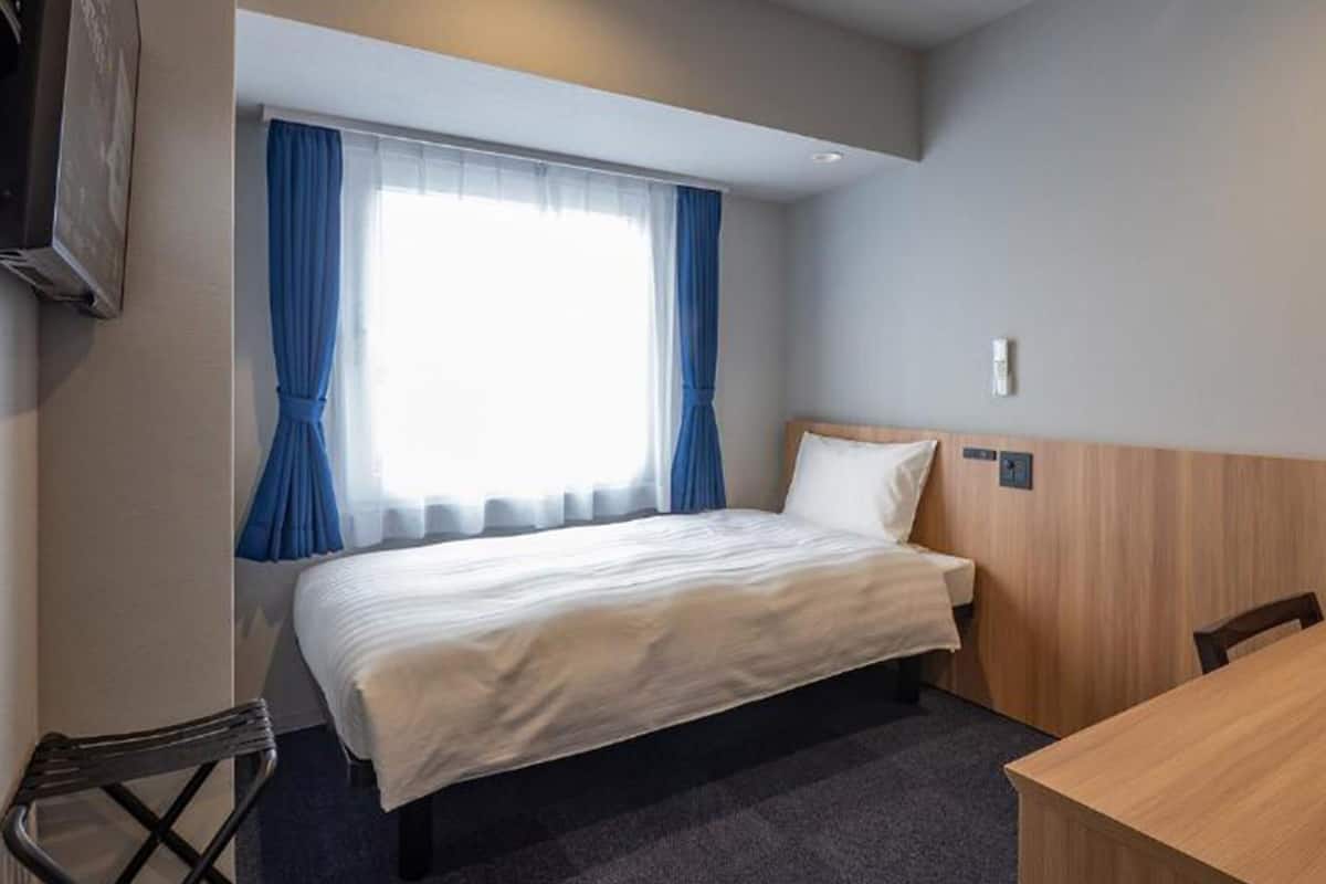 A hotel room with a bed, a desk, a chair, and a window with curtains.