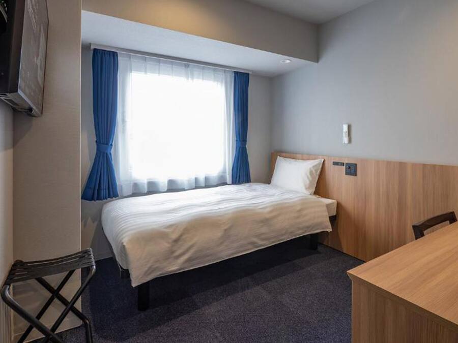 Ein Hotelzimmer mit Bett, Schreibtisch, Stuhl und einem fensterbehangenen Fenster.