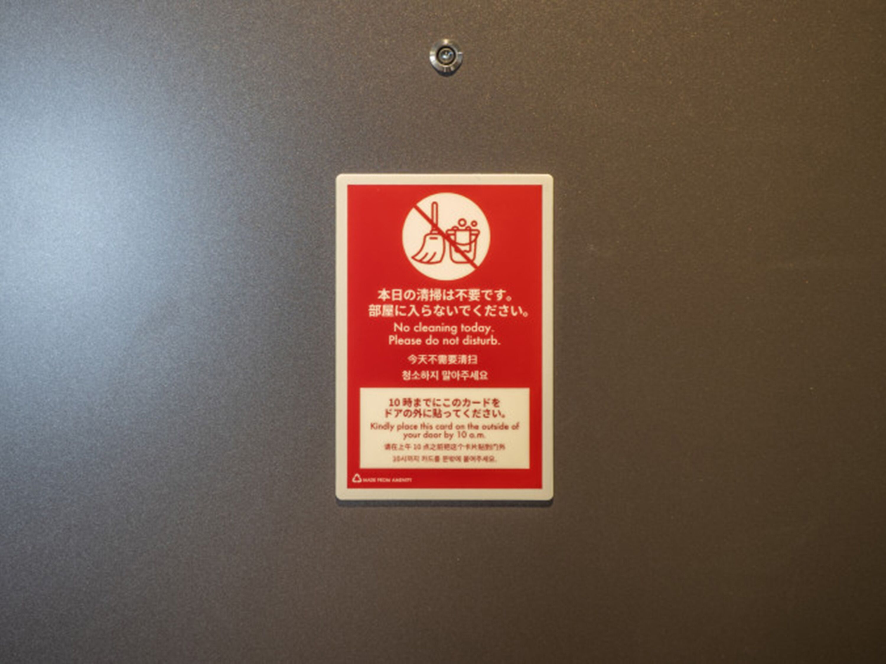Señal roja con texto y símbolos blancos en una puerta, indicando no hacer limpieza y solicitar no molestar.