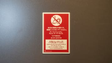 Señal roja con texto y símbolos blancos en una puerta, indicando no hacer limpieza y solicitar no molestar.