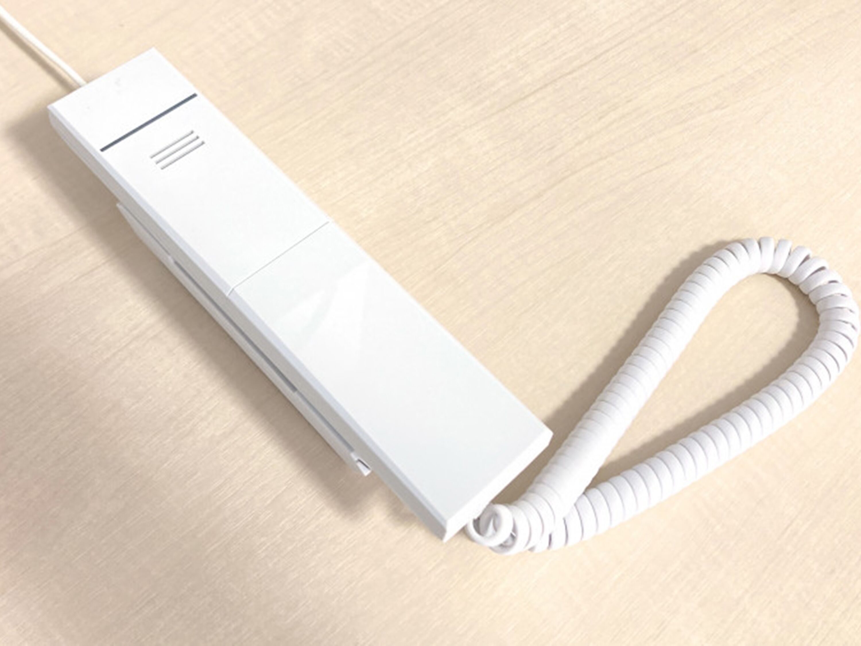 A white, rectangular device with a coiled cord on a wooden surface.
