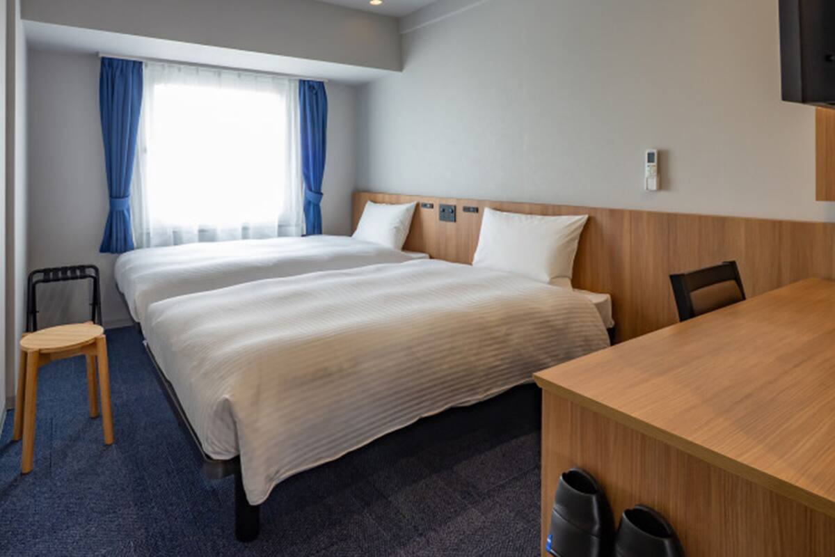 A hotel room with two beds, a desk, a chair, and a TV.