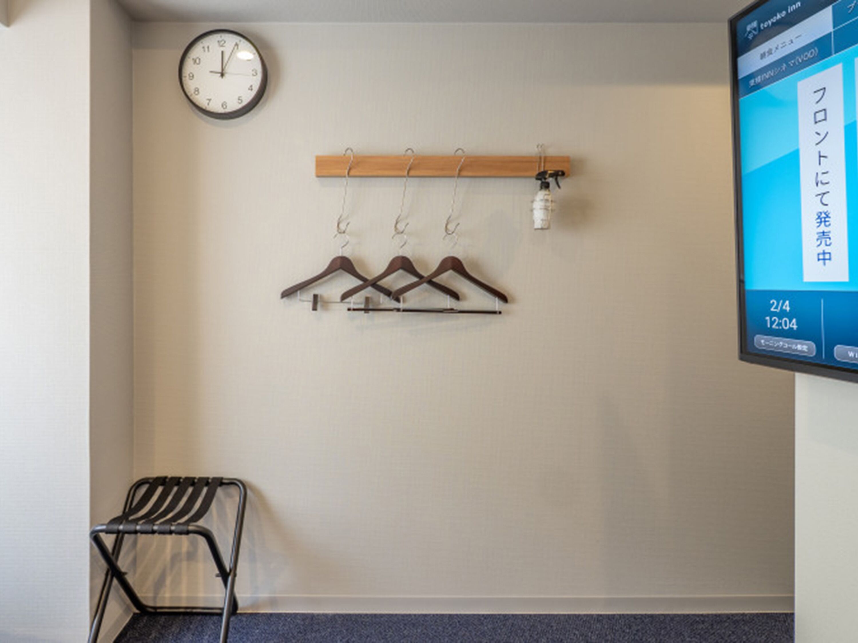 A room with a clock, a coat rack with hangers, a chair, and a digital display.