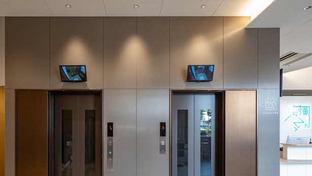 Two elevator doors with digital displays, a reception desk, and a sign with directional arrows. - Toyoko Inn Kure-eki (Kure)