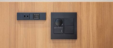 A wall-mounted control panel with a circular dial and two buttons, and a USB charging station with a power outlet.