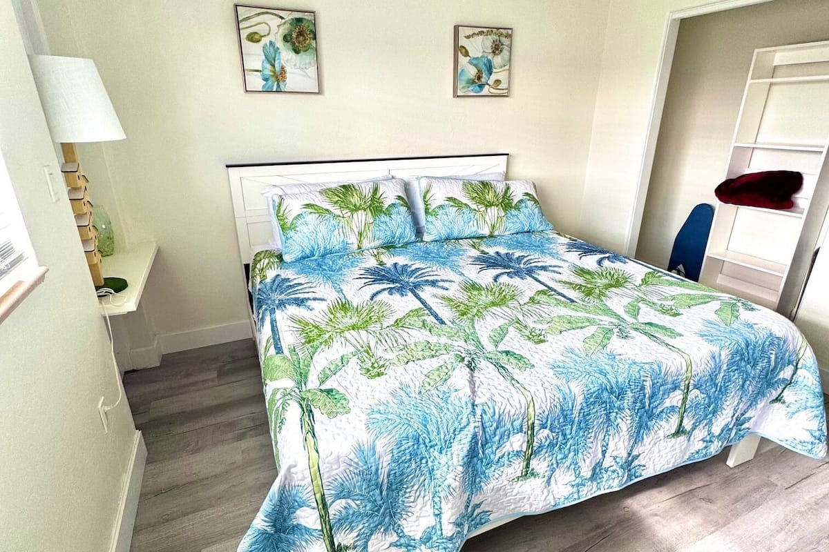 A bedroom with a bed, a ceiling fan, a nightstand, a lamp, and two wall-mounted pictures.
