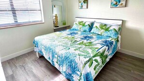 A bedroom with a bed, a ceiling fan, a window with blinds, and two wall-mounted paintings. - Penguins on the Beach Resorts 8 (Cocoa Beach)