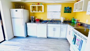 A kitchen with white cabinets, a refrigerator, a microwave, a toaster, and a window with blinds. - Penguins on the Beach Resorts 8 (Cocoa Beach)