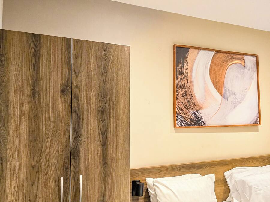 A bedroom with a wooden wardrobe, a bed with white bedding, and a painting on the wall.