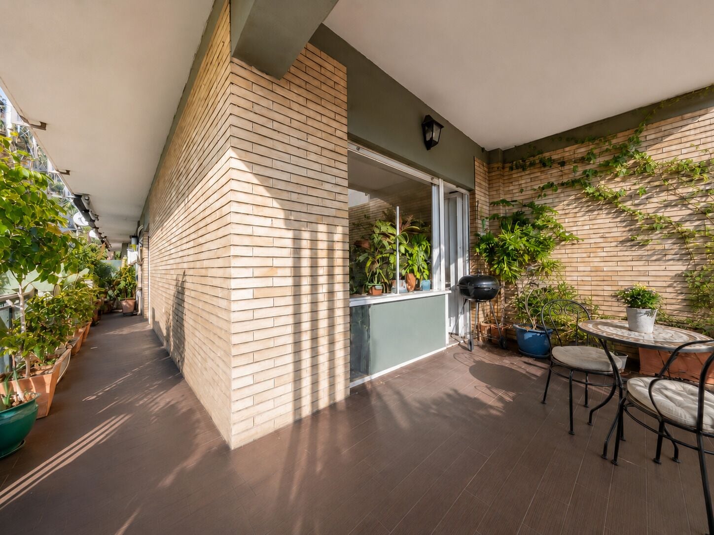 Un étroit couloir extérieur agrémenté de plantes en pot, d’un barbecue et d’une table ronde avec des chaises.