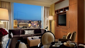 Une chambre d’hôtel dotée d’une grande fenêtre donnant sur la ville, d’une télévision, d’un canapé, d’un coin repas et d’une table d’appoint avec un plateau.