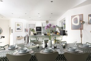 A modern dining area with a geometric patterned tablecloth, a central island with a vase of flowers, and a kitchen in the background.